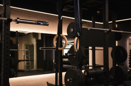 Close-up of wooden gymnastic rings hanging beside a weighted barbell in the gym