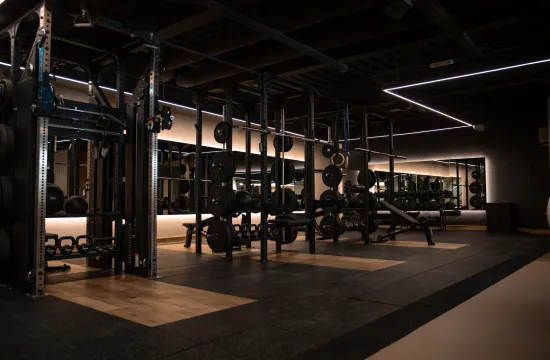 A dark gym area with weight racks, benches and mirrored walls lit by strip lighting