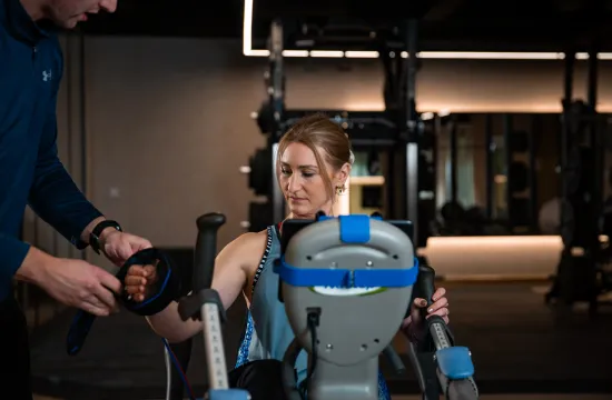 A trainer fits a compression cuff to a woman's arm as she sits on the Vasper System machine in the studio
