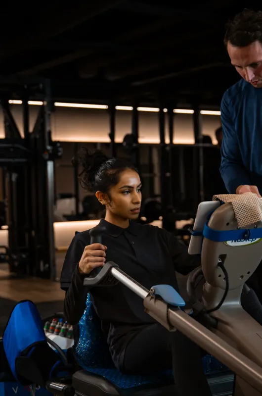 A trainer sets up the Vasper System's display for a seated client in the gym, with another client using a machine nearby