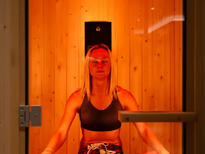 A trainer wearing a FIT top helps a smiling client into a BODY EMS training vest in the studio