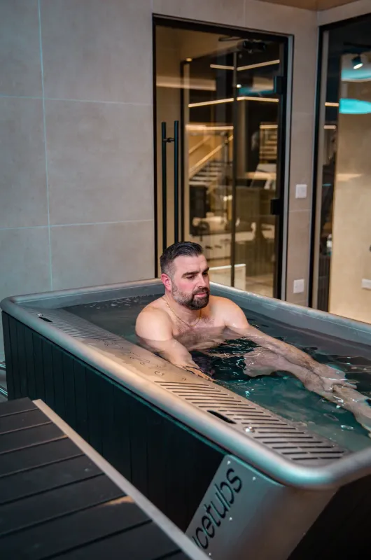 A man sitting in a cold plunge tub with his arms crossed, in a studio setting