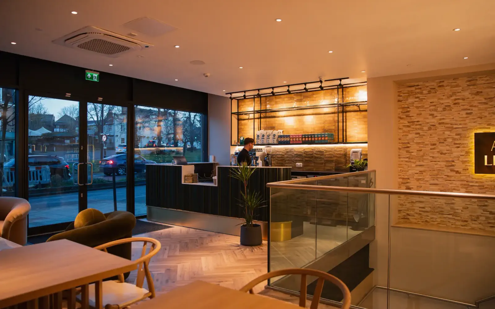 The FIT Partnership's café counter with a barista at work, tiled shelving stocked with drinks, and lounge seating by large windows