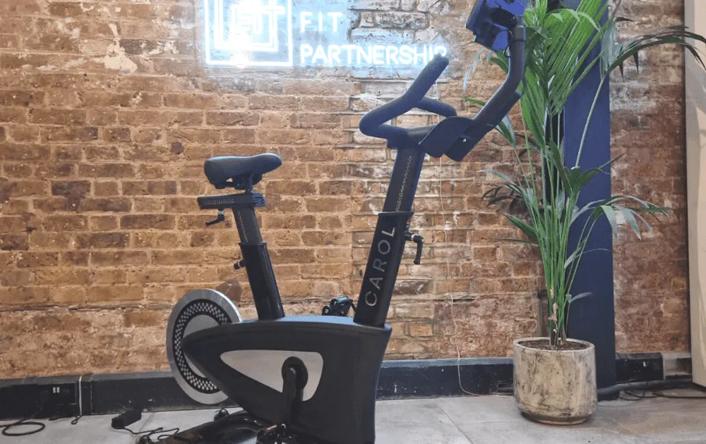 A CAROL exercise bike standing in front of The F.I.T Partnership's brick wall and neon sign