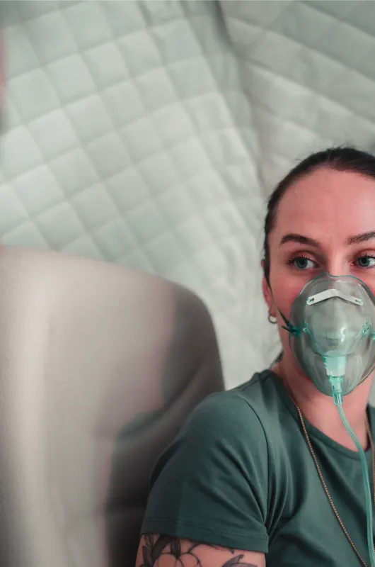 A woman wearing an oxygen mask sits inside a hyperbaric chamber beside the pod's control panel