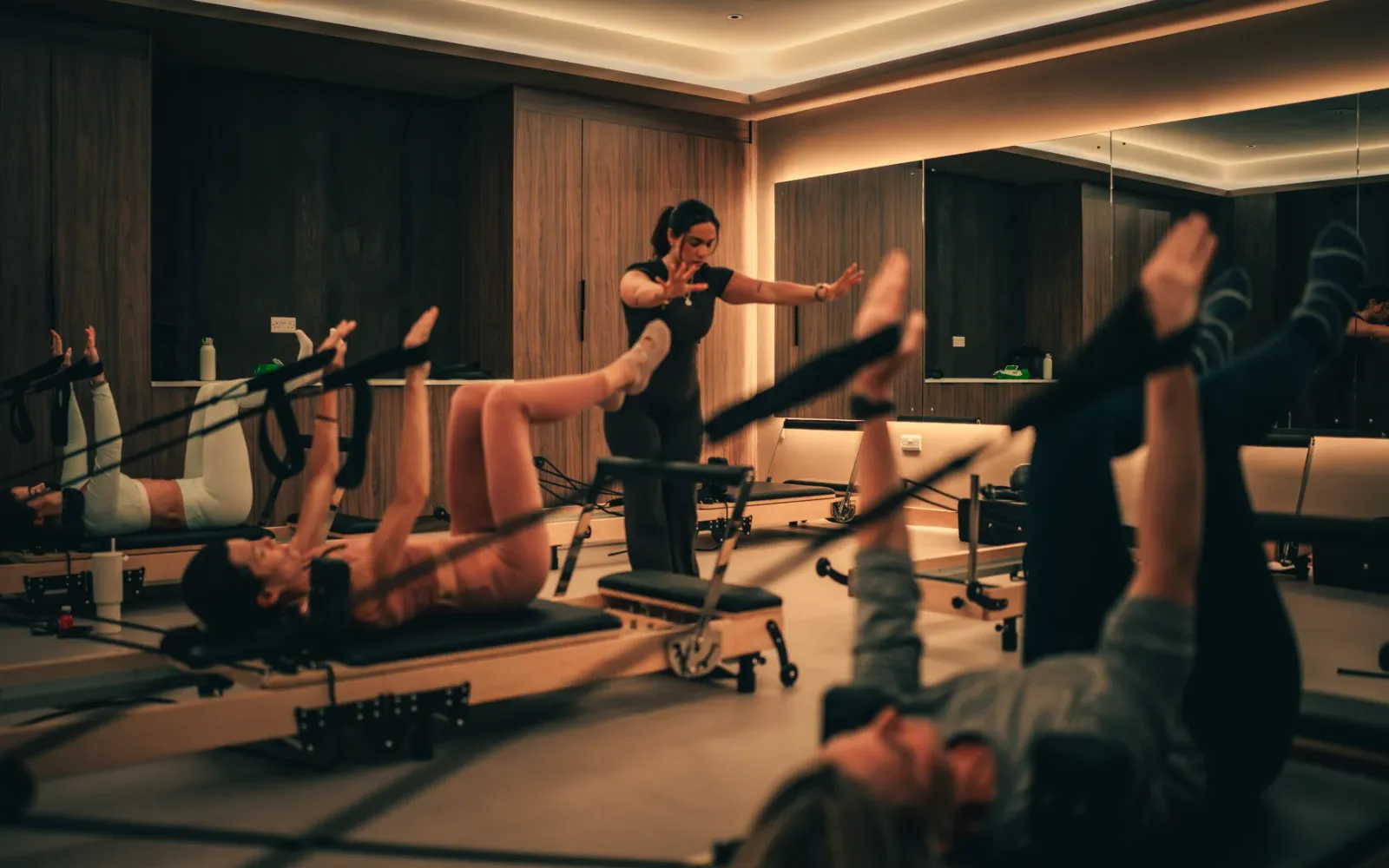 An instructor guides clients on reformer machines during a group Pilates class at The FIT Partnership studio in Esher