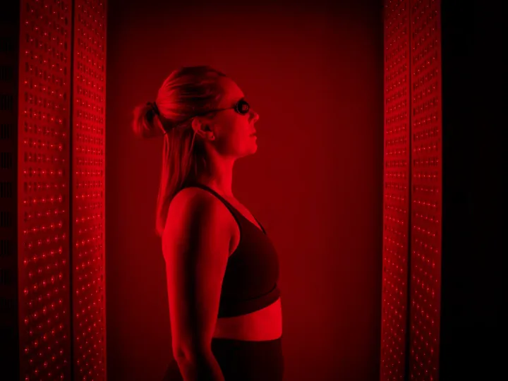 A woman in goggles stands between glowing red light therapy panels