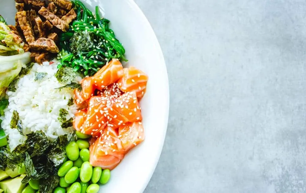 An overhead shot of a poke bowl with salmon, rice, edamame and seaweed