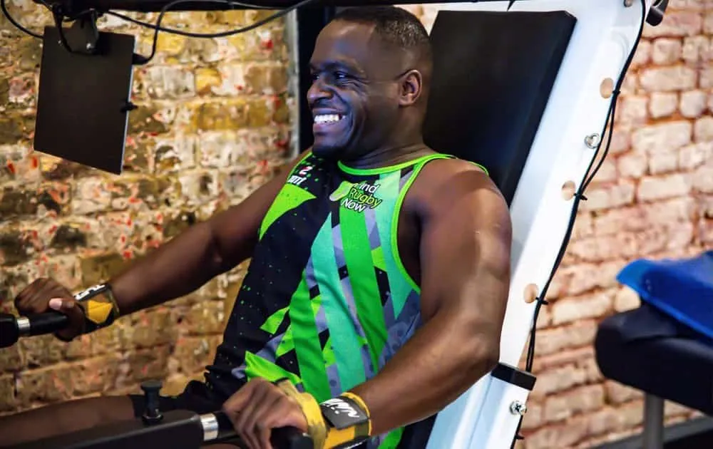 A man in a rugby vest smiling while using the Balkan Strength training machine