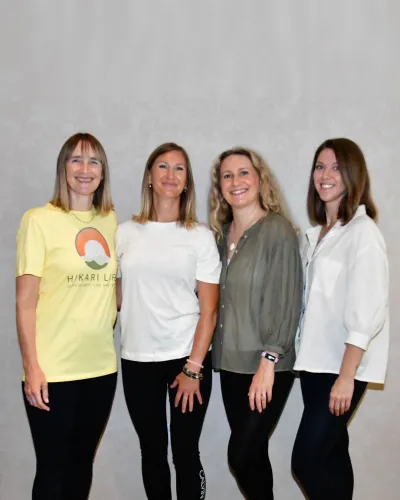 The four Hikari Life practitioners standing together against a plain grey backdrop, one wearing a yellow Hikari Life t-shirt