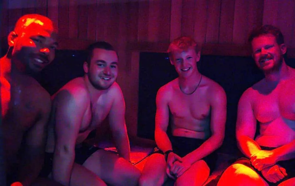 Four men sitting together smiling inside a red-lit infrared sauna