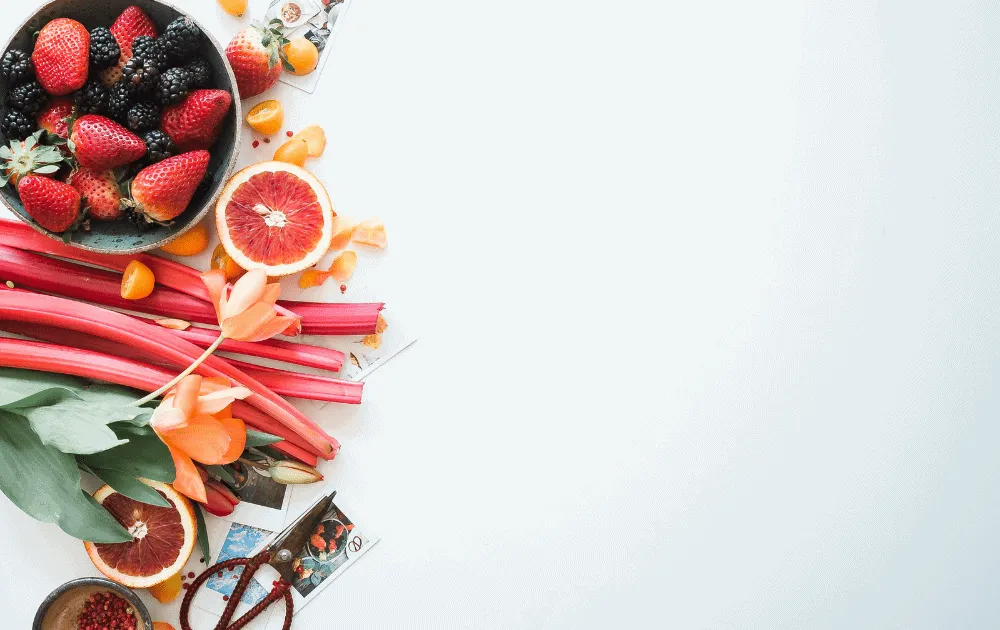 Fresh berries, blood oranges and rhubarb stalks arranged on a white surface