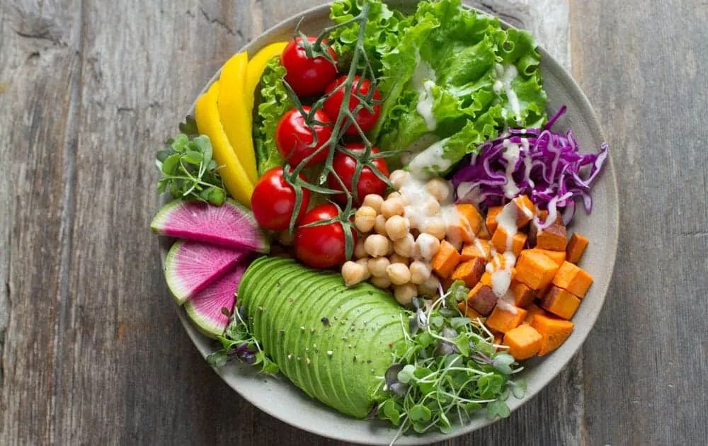 An overhead view of a bowl filled with avocado, cherry tomatoes, chickpeas, sweet potato and cabbage