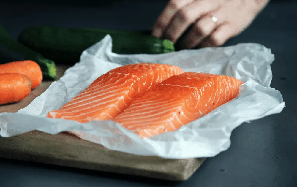 Two raw salmon fillets rest on parchment paper beside carrots and a courgette