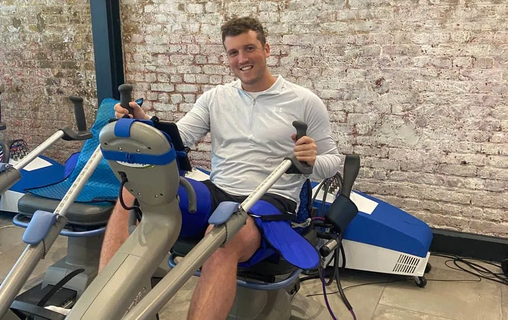 Man smiling while seated on a Vasper exercise machine against an exposed brick wall