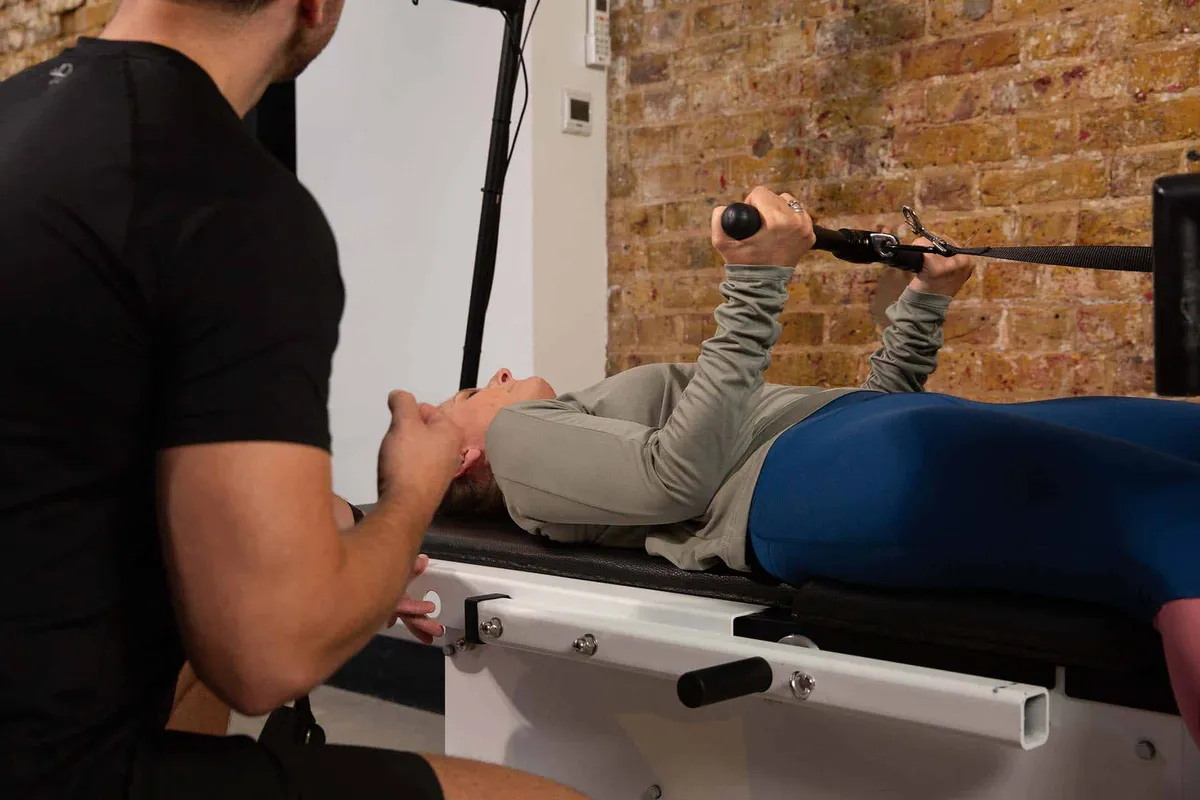 Trainer assisting a client using a cable resistance machine while lying on a bench