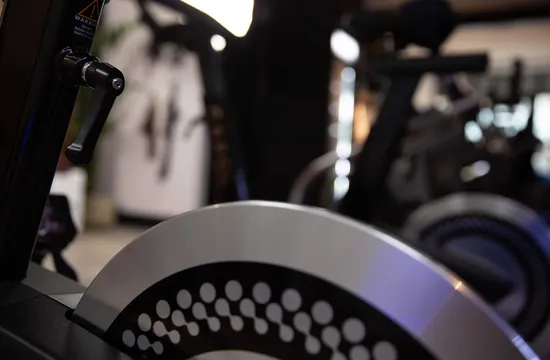 Close-up of the CAROL bike's flywheel with gym equipment blurred in the background