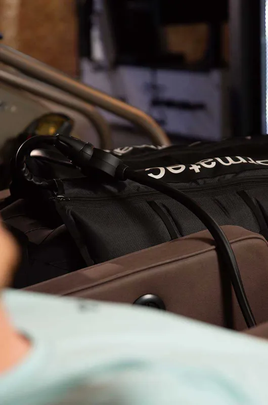 Close-up of a Normatec compression boot on a person's leg with the control hose attached