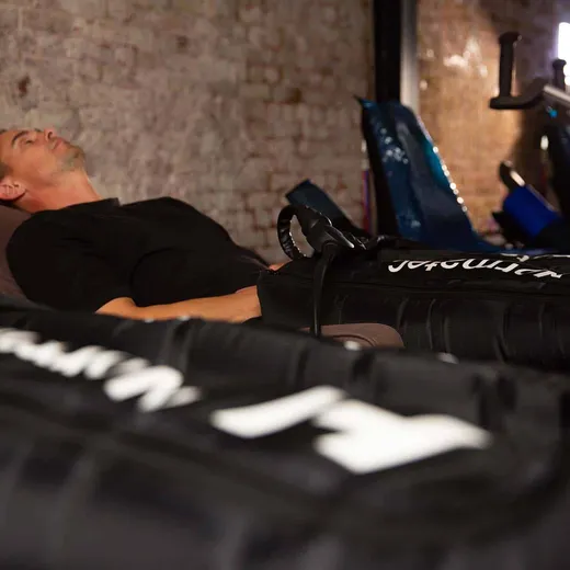 A man reclining in a treatment room while wearing compression therapy boots on his legs