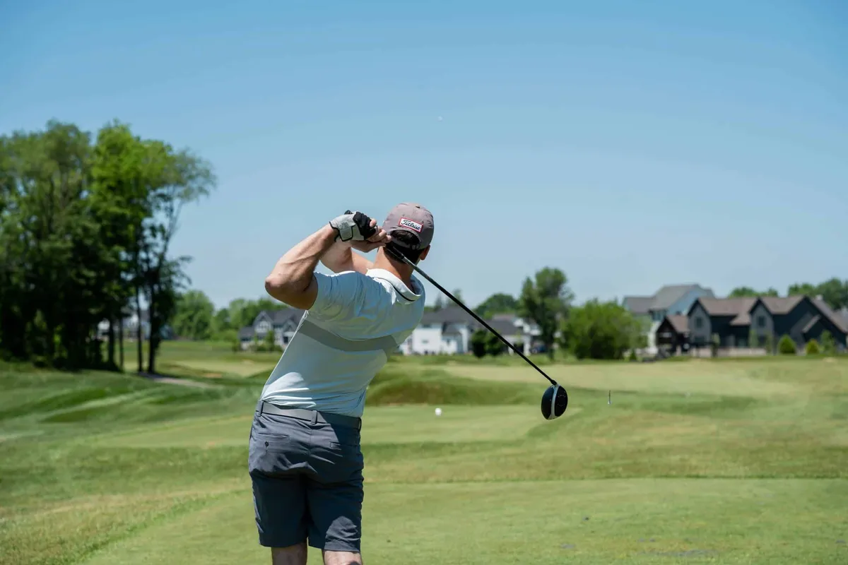 Golfer photographed from behind mid-swing on a course with houses in the background
