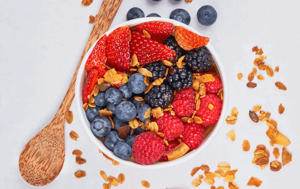 Bowl of granola topped with strawberries, blueberries, blackberries and raspberries
