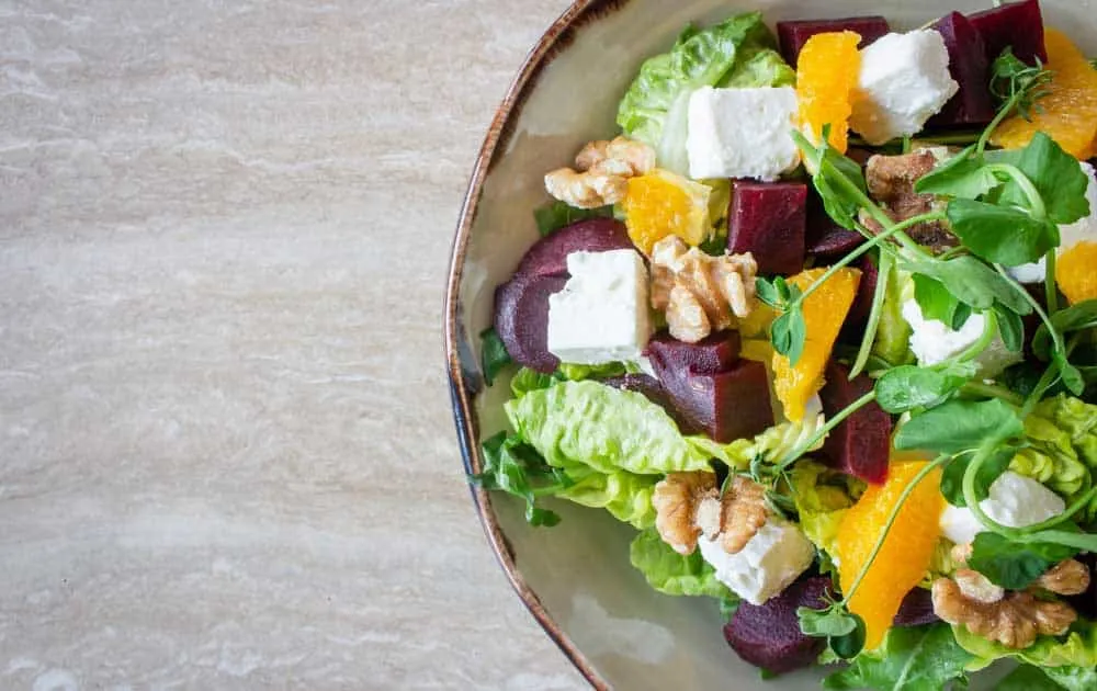 An overhead view of a salad with beetroot, feta, walnuts, orange segments and pea shoots