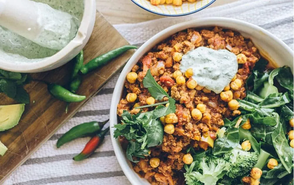 An overhead view of a bowl filled with spiced mince, chickpeas, greens and a herb yogurt dressing
