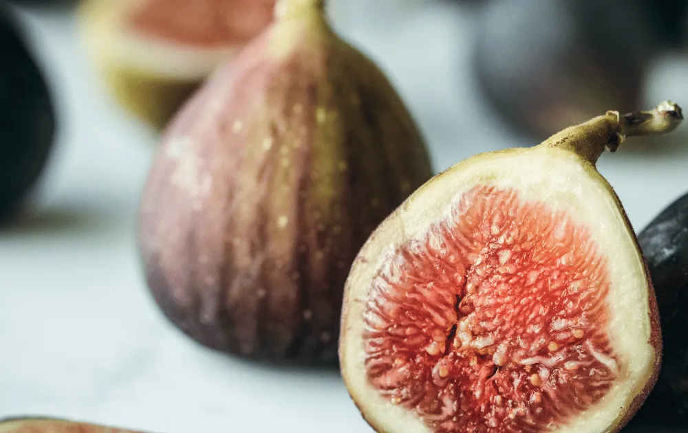 Halved fresh figs show their pink flesh beside whole figs on a table