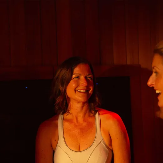 Two women smiling and chatting together inside a dimly lit sauna