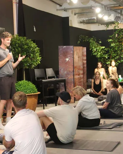 A speaker addresses attendees seated on mats during a workshop event at The FIT Partnership