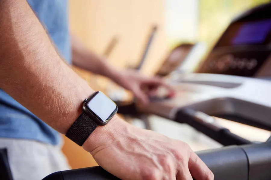 Close-up of a smartwatch on a wrist while its wearer exercises on a treadmill