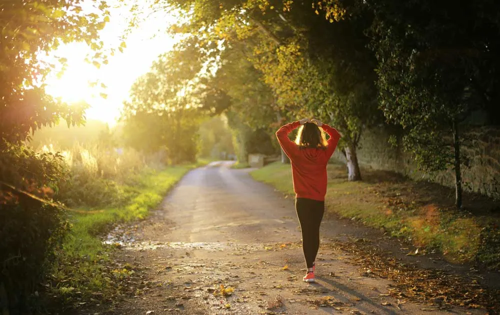 A woman jogging along a tree-lined path with her hands raised to her hair