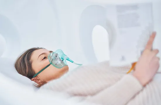 A woman lies back wearing a clear oxygen mask during a hyperbaric chamber therapy session