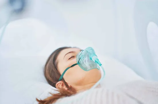 Close-up of a woman resting with her eyes closed while wearing an oxygen mask inside a hyperbaric chamber