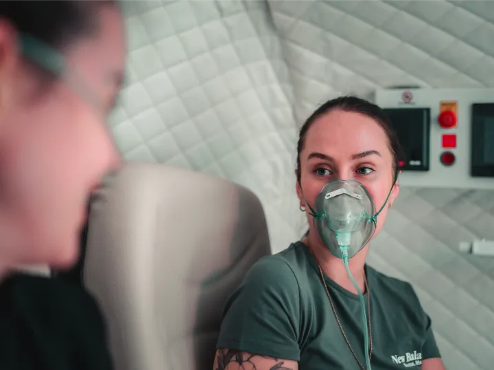 A woman relaxes in a hyperbaric oxygen chamber wearing an oxygen mask