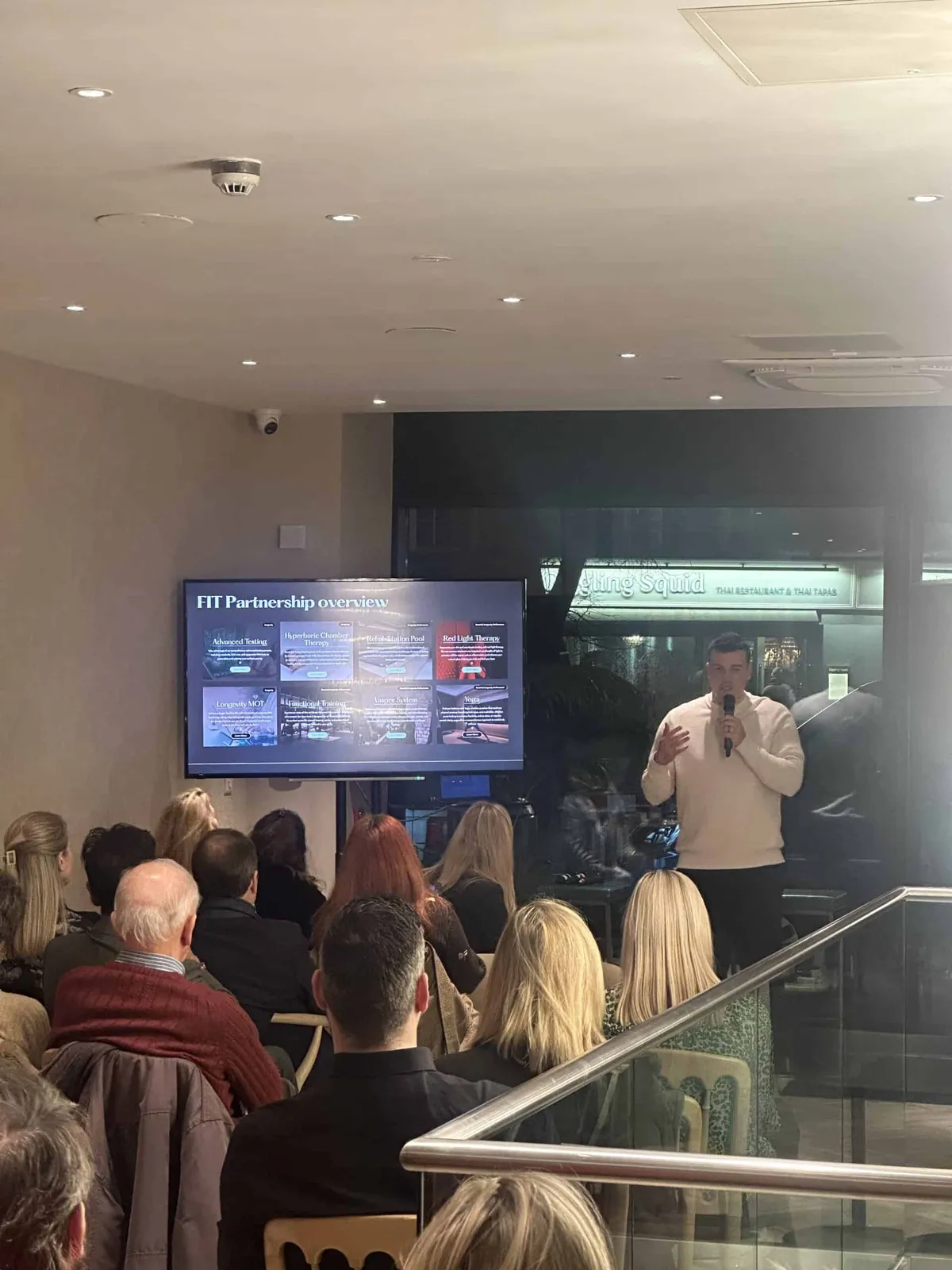 A man presents The FIT Partnership overview to a seated audience at the Esher wellness hub launch event
