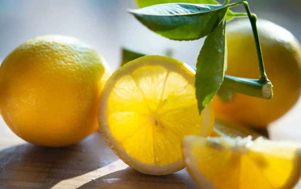 Whole and sliced lemons with green leaves rest on a wooden board