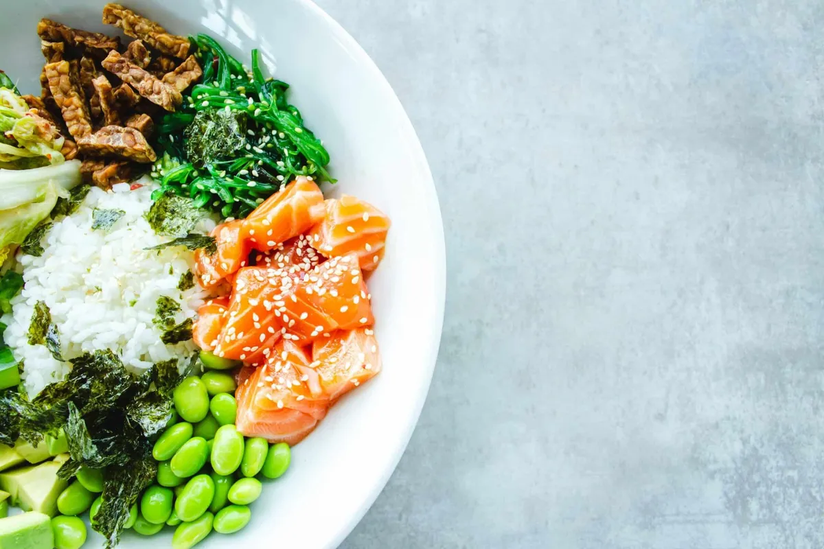 An overhead view of a poke bowl with salmon, rice, edamame, seaweed and greens