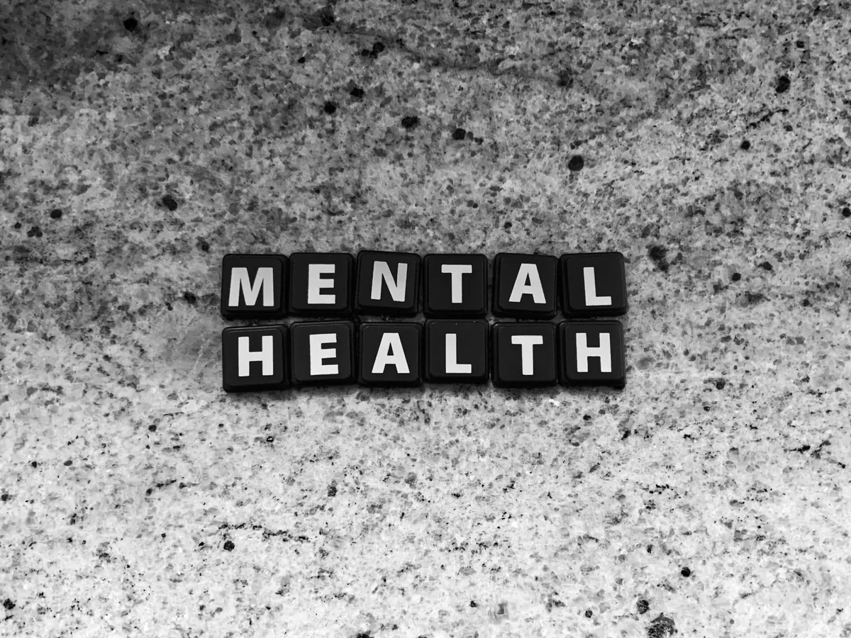 Black tiles spelling out 'mental health' on a speckled stone surface