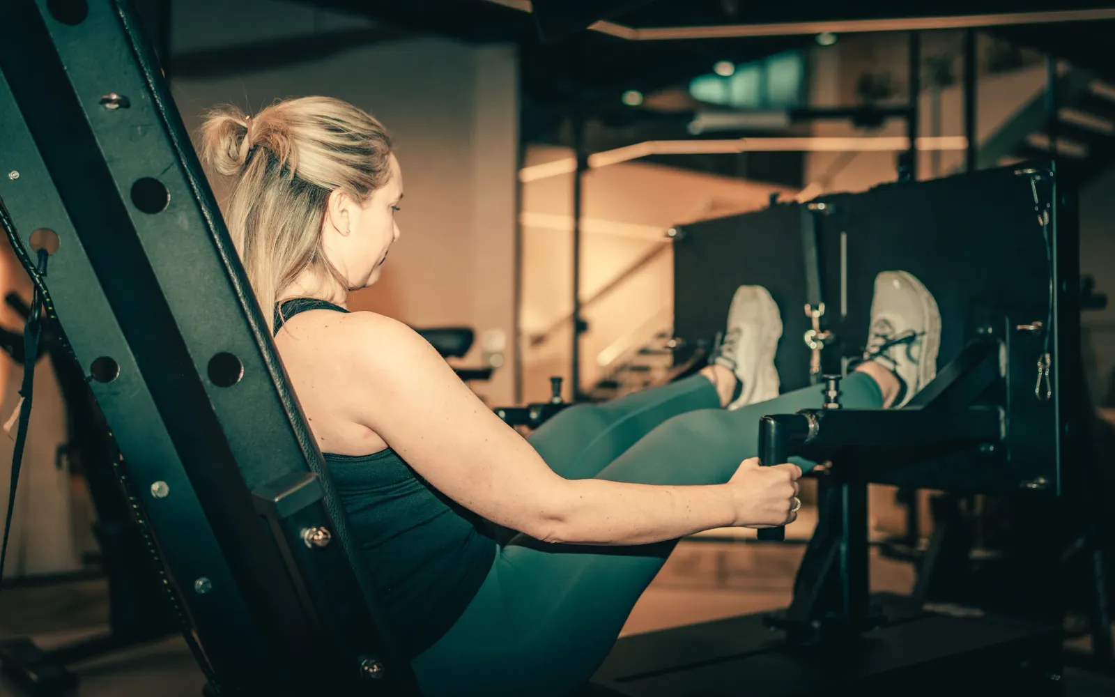 A woman in teal leggings drives against the footplate of the Balkan Strength Machine at The FIT Partnership, gripping its handles