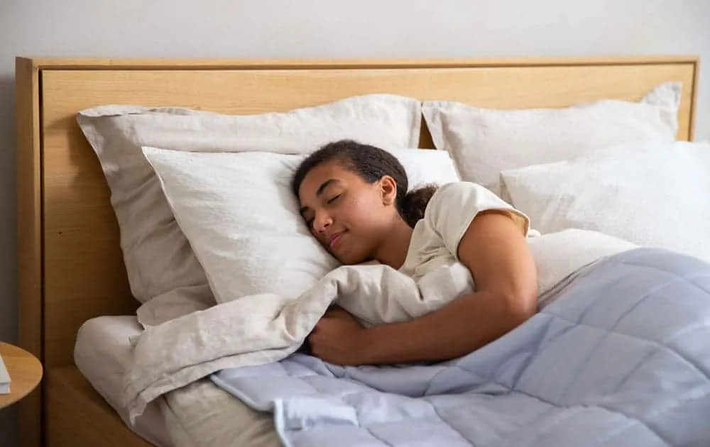 Woman sleeping soundly in bed, wrapped in a blanket with her face against a pillow