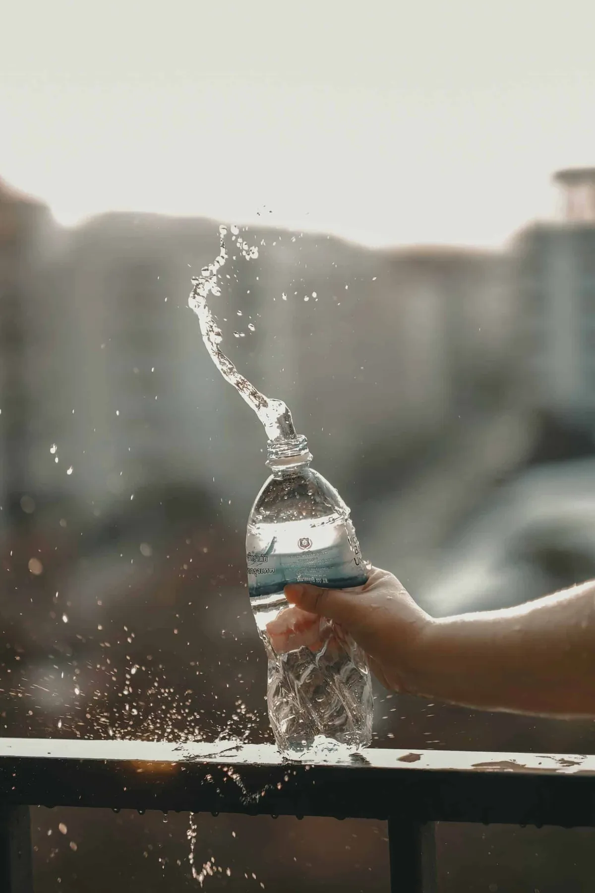 A hand squeezing a plastic water bottle, sending a splash of water into the air