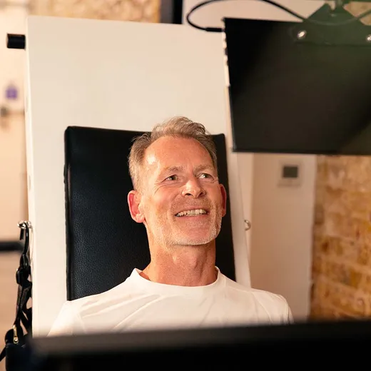 A smiling man reclines in the Balkan Strength Machine seat with its display monitor angled beside him