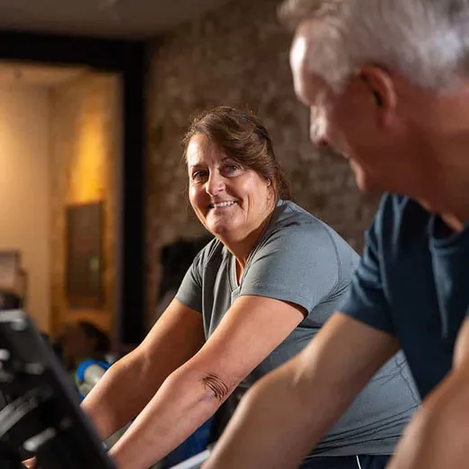 A smiling older woman cycling on a CAROL bike next to a man also riding beside her
