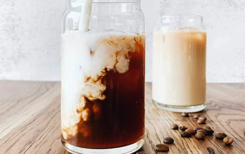 Two glasses of iced coffee made with plant based milk beside scattered coffee beans