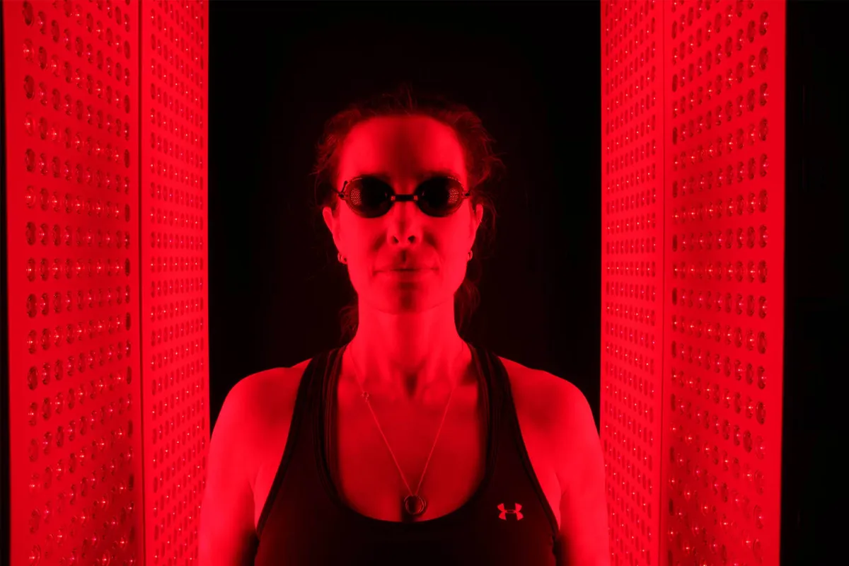 A woman wears protective goggles standing between glowing red light therapy panels