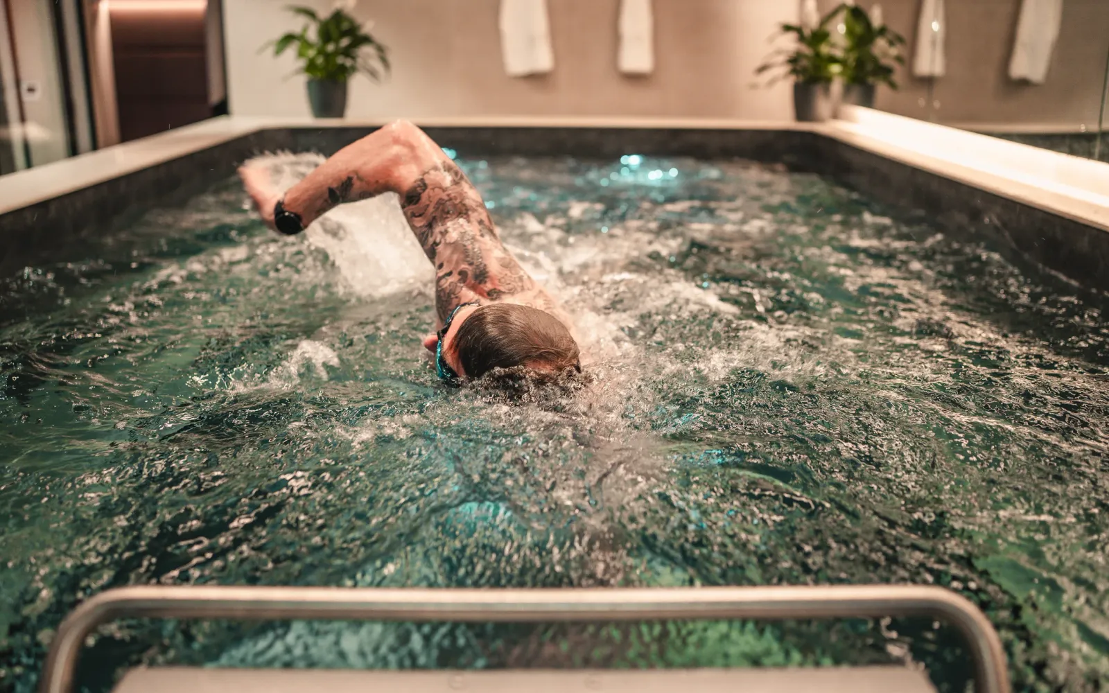 A swimmer powers through front crawl against the current of the endless pool at The FIT Partnership, with plants and towels on the ledge behind