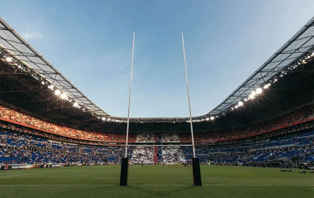 Rugby posts stand on the pitch of a packed stadium under floodlights