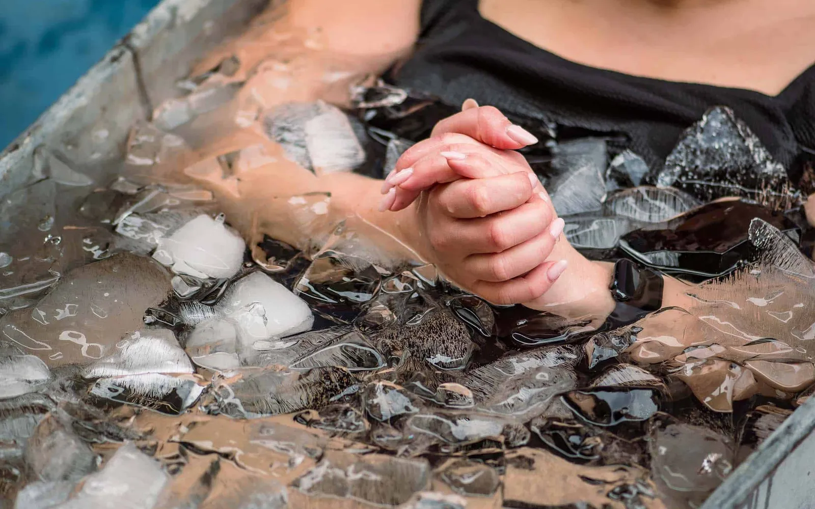 Two clasped hands submerged in an ice-filled cold plunge tub