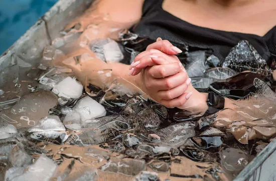Close-up of clasped hands submerged among ice cubes in a cold plunge tub